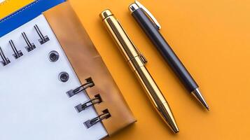 Close-up of a notebook with spiral binding and two pens on a vibrant orange background photo