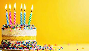 A birthday cake with lit candles on a yellow background photo