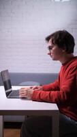 A man in glasses is working on computer at a table with a laptop video