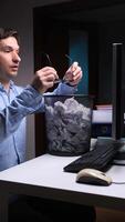 A man sitting at a desk with a computer and a trash can video