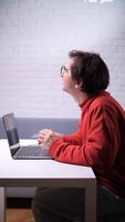 A man in glasses sits at a desk with a laptop video