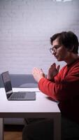 A man in glasses shows stop gesture at a table with a laptop video