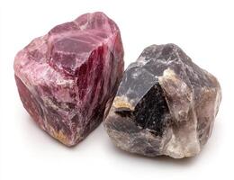 Two raw gemstones, one pinkish-red and the other gray-black, sit side-by-side on a white background. Detailed rock textures are visible photo