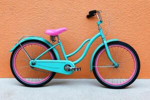 Teal bicycle with pink accents against an orange wall photo