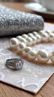 A silver necklace, pearl necklace and a ring sit on a table photo