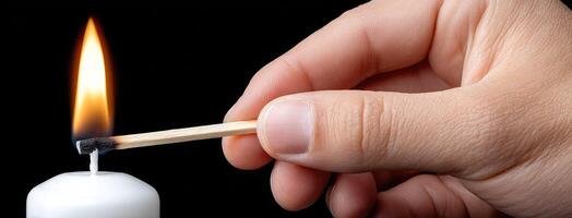 A person holding a matchstick over a lit candle photo