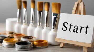Paint brushes and paint on easel with start sign photo