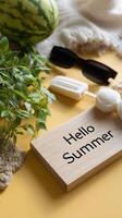 Hello summer sign on a wooden plate with a watermelon, sunglasses, and a beach towel photo