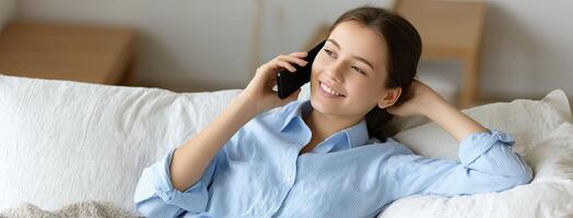 A woman is laying on a couch and talking on a cell phone photo