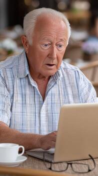 An older man sitting at a table with a laptop photo