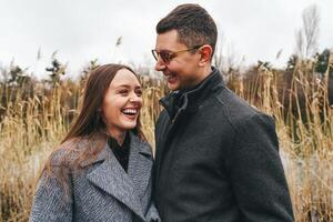 Couple enjoying a joyful moment by a serene lake surrounded by tall grass on a cloudy day in early spring photo