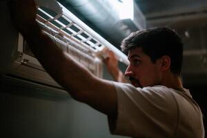 Technician repairing an air conditioning unit in a modern indoor setting during evening hours photo