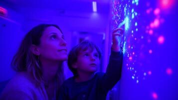 Mother and child exploring colorful light patterns in an interactive space during an evening visit photo