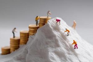 Figurines scaling a mountain of coins as they conquer financial challenges in a creative representation of success photo