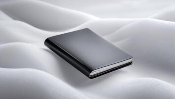 Black notebook resting on a soft, white surface with gentle curves in a tranquil setting photo