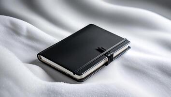 Black notebook resting on soft white fabric in a cozy setting, ideal for writing reflective thoughts or brainstorming ideas photo