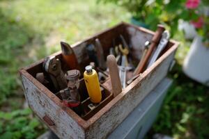 Rustic toolbox filled with various hand tools resting on a grassy surface during midday photo