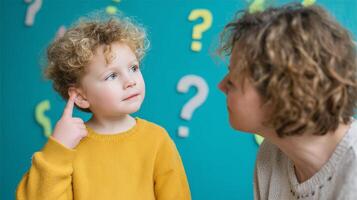 Child with curly hair listens intently to adult in a colorful learning environment with question marks on the wall photo