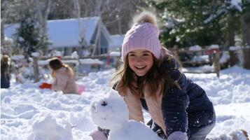 Smiling girl builds a snowman in a winter wonderland with friends in a snowy landscape during daytime photo
