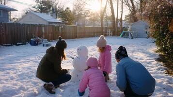 Family enjoys a winter afternoon building a snowman in their backyard under the warm glow of a setting sun photo