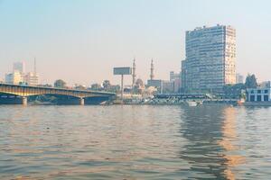 View of Cairo skyline with mosques, buildings, and a bridge reflected in the Nile River during the golden hour photo