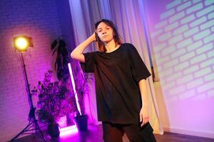 Person posing confidently in a creative space with colorful lighting and plants in the background during an artistic showcase photo