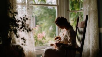 Mother nurses baby in rocking chair by the window in a sunlit room surrounded by plants and soft curtains photo