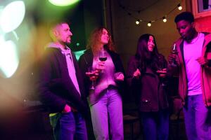Group of friends enjoying a lively evening outdoors with drinks under string lights in a vibrant setting photo