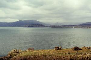 Cloudy sky over a tranquil lake with distant mountains and rocky shoreline photo