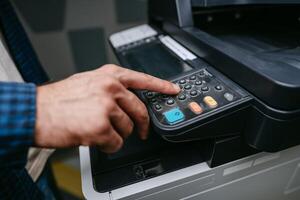Man using a multifunction printer to operate the control panel in an office environment during working hours photo