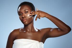 Woman applying skincare product on her face in a studio setting with soft blue background photo