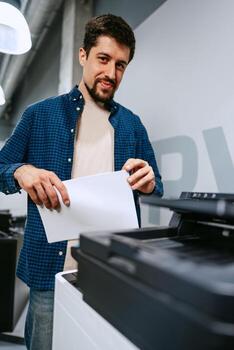 Man operates printer in modern office space while preparing printed documents for work tasks photo
