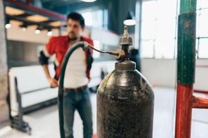 Worker inspecting a gas cylinder in a modern workspace during daylight hours photo