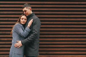 Couple embraces against wooden wall in urban setting, capturing a moment of intimacy and connection during a cool day photo