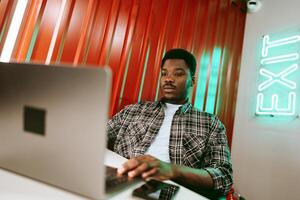 Young man working on laptop in a modern workspace with vibrant red walls and bright exit sign at evening photo
