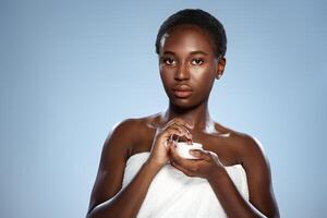 Woman applying cream while wearing a towel, capturing essence of skincare routine against a blue background photo