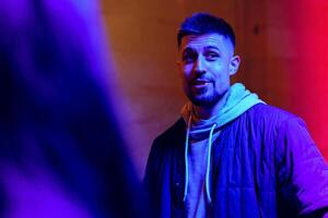 Young man engaging in conversation under colorful lights in an urban setting during night hours photo
