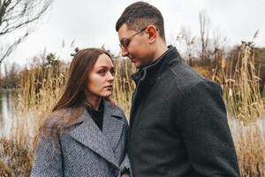 Couple sharing an intimate moment by the lake surrounded by tall grass on a cloudy day photo