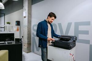 Man operates a printer in a modern office environment during daylight, focused on completing tasks efficiently and professionally photo