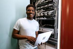 Young professional managing servers with laptop while smiling in a data center during daytime photo
