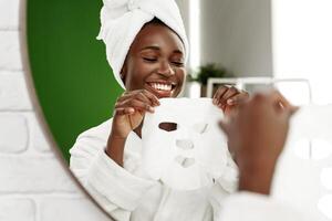 Woman applying a facial mask while smiling in a bathroom setting with a mirror reflection photo