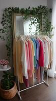 Colorful sweaters hanging on a rack by a mirror in a cozy indoor space surrounded by greenery photo