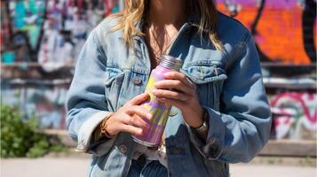 Woman holds colorful drink can in urban setting with vibrant graffiti background during sunny day photo