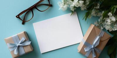 Presents with blue ribbons and blank card placed on a turquoise surface surrounded by flowers and eyeglasses photo