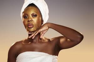 Woman relaxing with a gold face mask while wrapped in a towel in a serene spa-like setting during a beauty routine photo