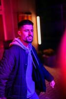Young man walks confidently in vibrant urban nightlife, illuminated by neon lights in an evening setting photo