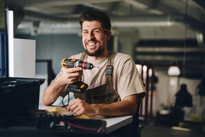 Smiling craftsman holds drill while working in workshop during the day photo