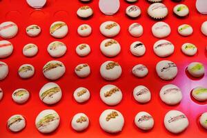 Colorful macarons arranged neatly on a bright red display reflecting an artful pastry shop environment photo