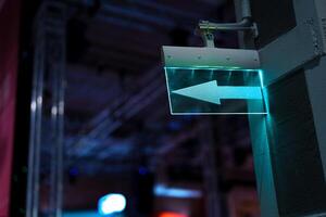 Directional sign illuminated in teal as it guides visitors in an indoor event space during nighttime activities photo