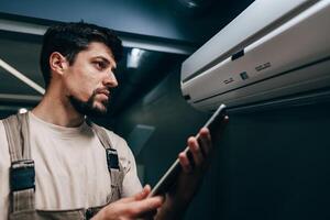 Technician inspects air conditioning unit while checking readings on a tablet in a modern indoor space photo